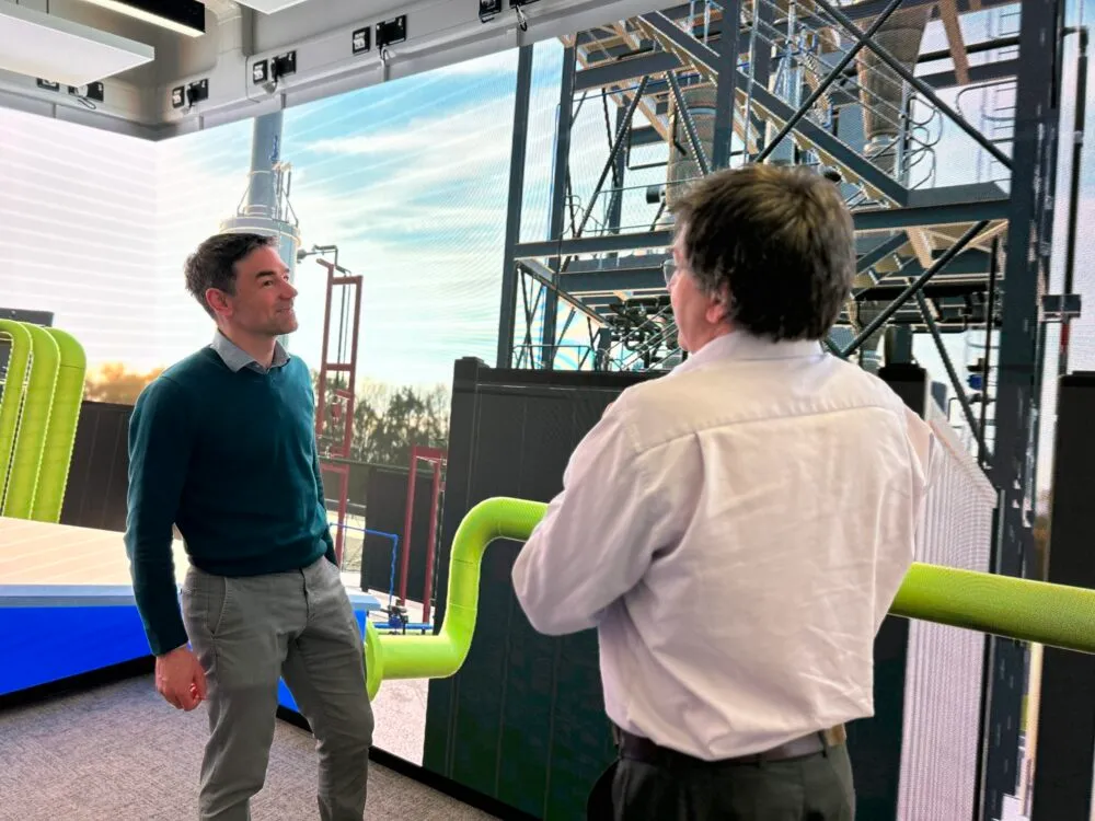 Two people talking in front of a very large computer display screen